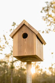 a wooden birdhouse sitting on top of a pole in front of some trees and grass