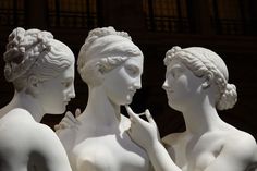 three white statues are standing next to each other in front of a building and one is touching her lips