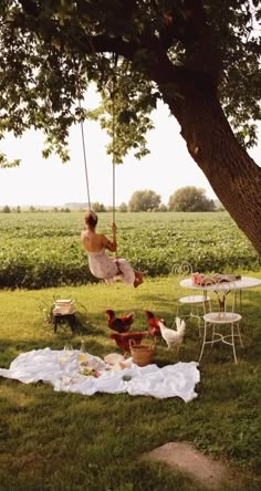 a woman sitting on a swing in the middle of a field with chickens and hammocks