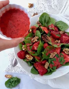 a person is holding a bowl of strawberries and spinach salad with walnuts