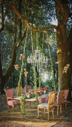 an outdoor dining area with chairs, table and chandelier hanging from the trees