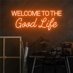 a neon sign that says welcome to the good life in front of a desk and chair