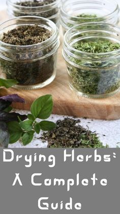 four jars filled with herbs sitting on top of a wooden cutting board next to green leaves