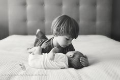 a little boy laying on top of a bed next to a baby