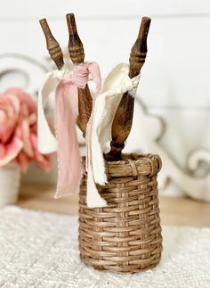 two wooden sticks sticking out of a wicker basket on a white rug next to pink flowers