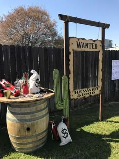 a wooden sign sitting on top of a grass covered field next to a barrel filled with bags