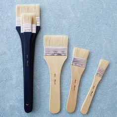 three paint brushes lined up next to each other on a blue surface with one brush in the foreground