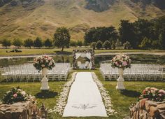 an outdoor wedding ceremony setup with white chairs and flowers on the aisle, surrounded by mountains