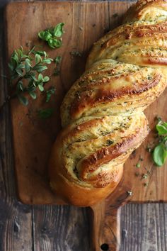 a loaf of bread sitting on top of a wooden cutting board next to a sprig of green leaves