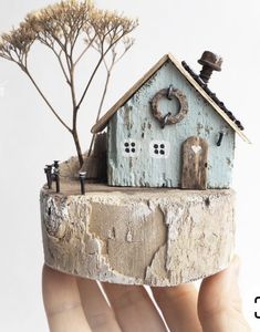 a hand holding a miniature house made out of wood and concrete with trees in the background