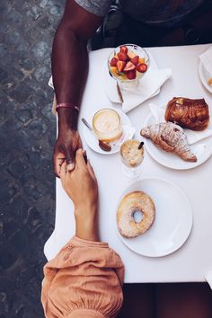 two people sitting at a table with plates of food and drinks on it, one holding the other's hand