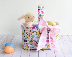 a stuffed bunny sitting in a basket next to an easter egg on a white table