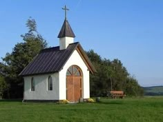 a small white church with a cross on it's roof in the middle of a field