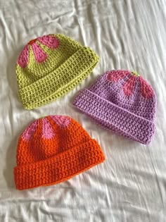 three crocheted hats laying on top of a bed