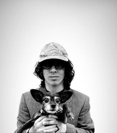 a man holding a small dog in his arms and wearing a hat on top of him