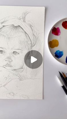 a drawing of a child's face on paper next to markers and paintbrushes