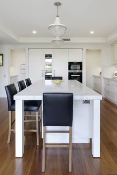 a large kitchen with white cabinets and black leather chairs in front of an island counter