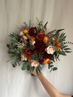 a person holding a bouquet of flowers on a white background with leaves and foliage in the foreground