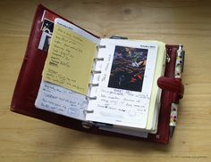 an open notebook with notes and pictures on it sitting on top of a wooden table