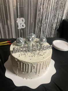 a birthday cake with white frosting and silver decorations on a black tablecloth covered table