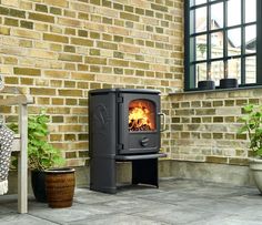 a wood burning stove sitting on top of a patio next to a brick wall and potted plants