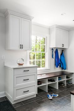 a kitchen with white cabinets and gray tile flooring next to a window that has blue jackets hanging on it