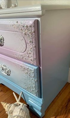 a blue dresser with silver glitter on it and a seashell sitting next to it