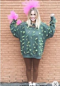 a woman standing in front of a brick wall wearing a green sweater with pink flowers on it