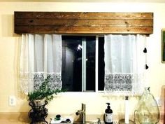 a kitchen sink under a window with white curtains and lace on the valance above it