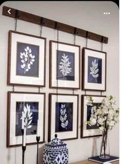 four framed pictures hang on the wall above a dresser with flowers in vases and candles