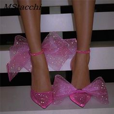 a pair of pink shoes with glitter bows on the toes and ankles, sitting on a white surface