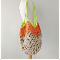 an orange and white crochet bag on a mannequin head stand with a green handle