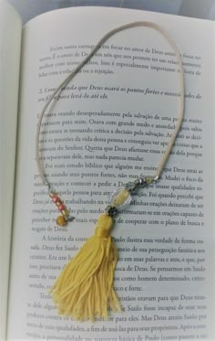 an open book with a tasseled yellow necklace on it's side and beads hanging from the end