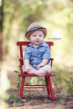 a baby sitting in a red chair with a hat on it's head and wearing a blue shirt