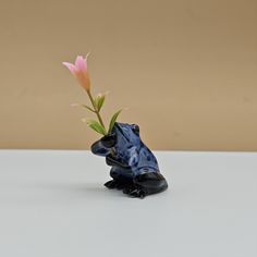 a blue frog figurine holding a pink flower