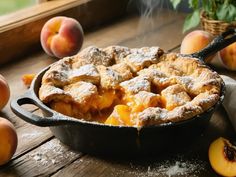 a skillet filled with fresh peach cobble next to sliced peaches on a wooden table