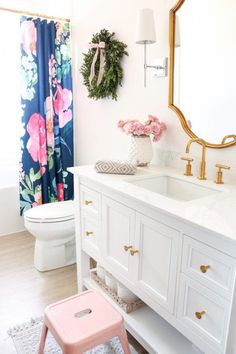 a white bathroom with floral shower curtain and pink stool in front of the vanity sink