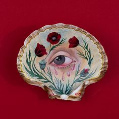 a decorative plate with an eye and flowers painted on the side, against a red background