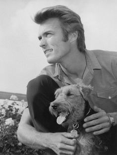 a black and white photo of a man holding a dog in his lap while smiling