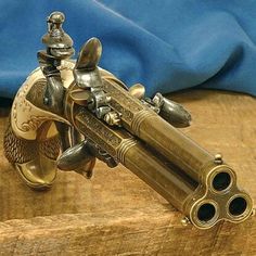 an antique brass revolver on a wooden table next to a blue cloth and some metal fittings