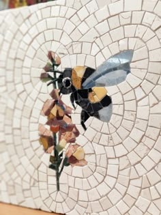 a mosaic tile wall with a bee and flower on it's side, in the center