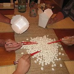 several people are sitting at a table with chopsticks and marshmallows