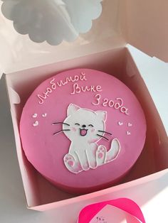 a pink cake in a box with a cat design on the top and writing on the side