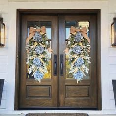 two wreaths on the front door of a house with lights hanging above them and an entrance mat