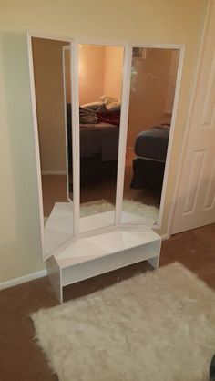 a room with a bed, mirror and white shelf in the corner on carpeted floor