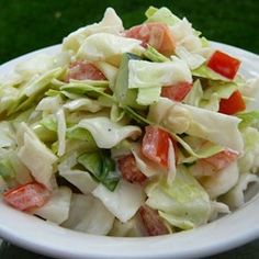 a salad with lettuce and tomatoes in a white bowl on a green table