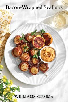 a white plate topped with food next to a glass of wine and flowers on top of a table