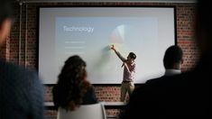 a man standing in front of a projector screen giving a presentation to people sitting around