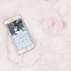 an iphone is hooked up to ear buds on a white fur surface with pink pom - poms