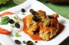 two enchiladas on a white plate topped with sour cream and black olives